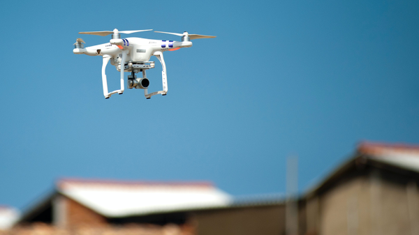 A drone flying over a set of houses. The camera is focused on the drones, while the neighborhood is blurred.