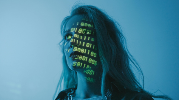 A woman in a blue-lit room with green lines of code projected onto her face for an AI girlfriend.