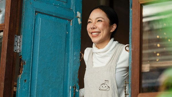A woman looking out from a weathered blue door of her business. Business practices help keep it afloat.