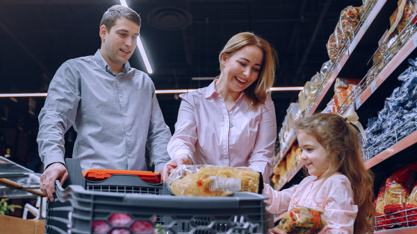 A dimmed sensory friendly view of a family inside of a grocery store , a man, woman, and young girl looking at groceries to go into a cart.