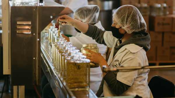 Several humans in protective gear working on a production line with various liquids in bottles, including a deaf worker.