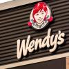 An outdoor sign of a Wendy's restaurant, focusing on the logo and top of the roof.