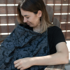 A woman with a breastfeeding baby sitting under a privacy cloth while she sits outside.