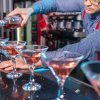 A person pouring red alcohol into a line of martini glasses on a counter, passing by a case for sexual harassment.