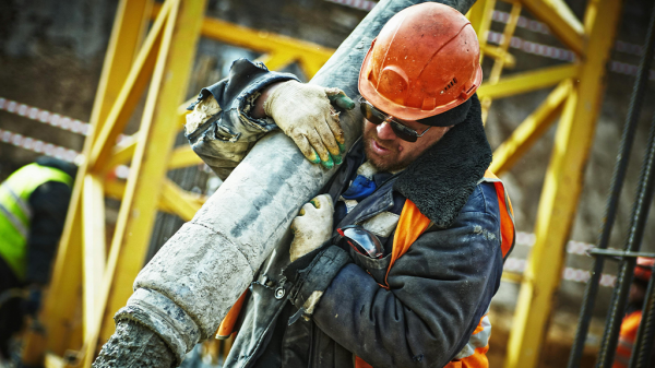 A man lifting a girder on a construction site, wearing a hard hat and a name tag to avoid misclassification.