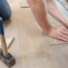 A person installing flooring in a house, measuring and marking a corner with a pencil with a hammer nearby, reviewing OSHA regulations.
