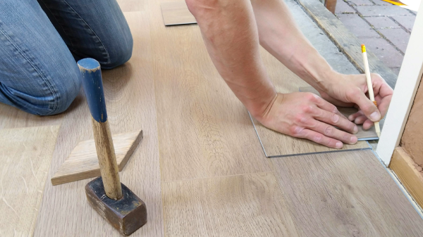 A person installing flooring in a house, measuring and marking a corner with a pencil with a hammer nearby, reviewing OSHA regulations.