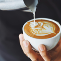 A person pouring oat milk onto the top of coffee with latte art that fits ADA compliance.