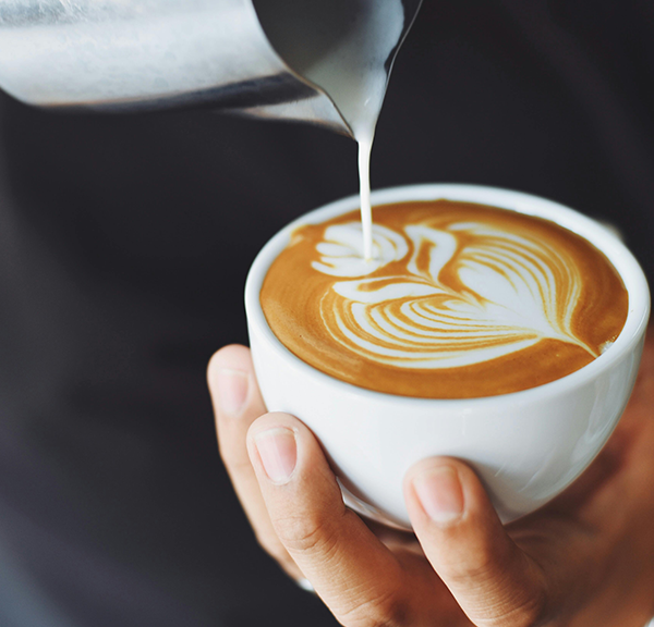 A person pouring oat milk onto the top of coffee with latte art that fits ADA compliance.