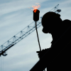 A silhouette of a construction contractor in the early morning as they carry a flaming torch.