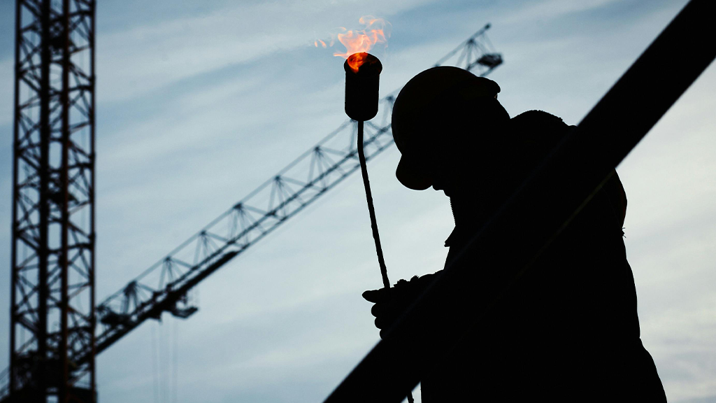 A silhouette of a construction contractor in the early morning as they carry a flaming torch.