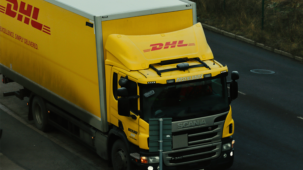 A yellow DHL truck driving along a road on a cloudy day.