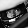 A close up of a man inside a motorsport helmet and vehicle, with grayscale overlaid.