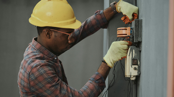 A Black man working on an electrical apparatus on the wall for Stanley Black + Decker.
