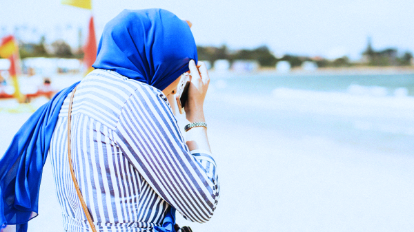 A woman wearing a blue head covering for religious accommodation and blue pinstripe suit standing on a beach.