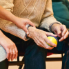 An older person with a supportive stress ball in one hand and having a second person hold their hand in nursing care, supported by OSHA rules.