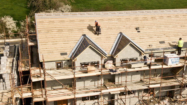 A large house in construction being roofed and following OSHA safety guidelines with two men safely on the roof.