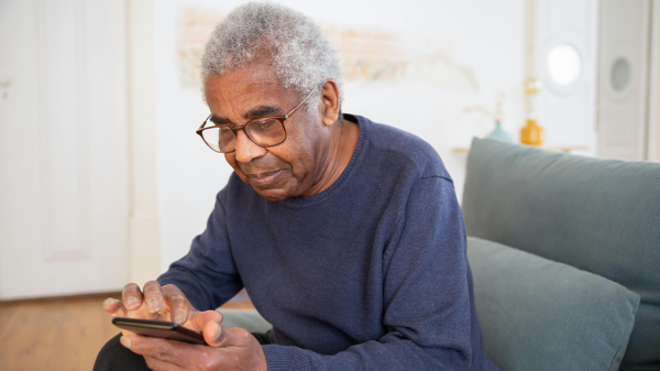 A senior Black man looking at a smartphone, reading about online scammers.