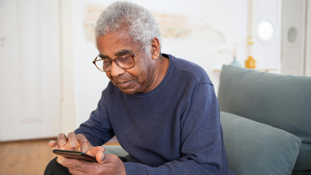 A senior Black man looking at a smartphone, reading about online scammers.