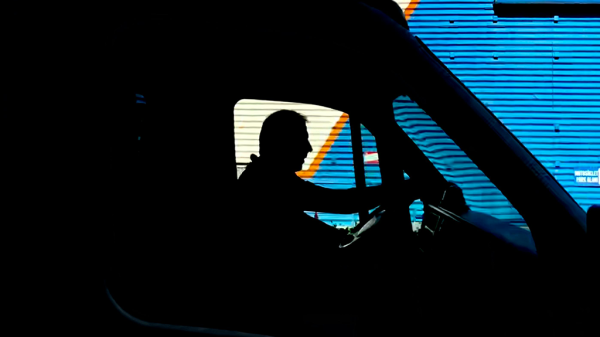A silhouette of an amputee driving a truck, with a blue metal wall behind them.