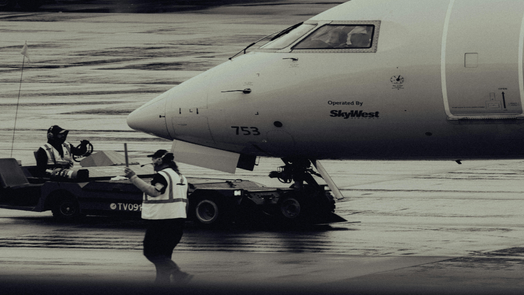A group of airplane workers managing an airplane on the tarmac following OSHA safety guidelines.