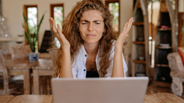 A woman with long curly hair looks at a laptop in front of her with an exasperated expression going through search results.
